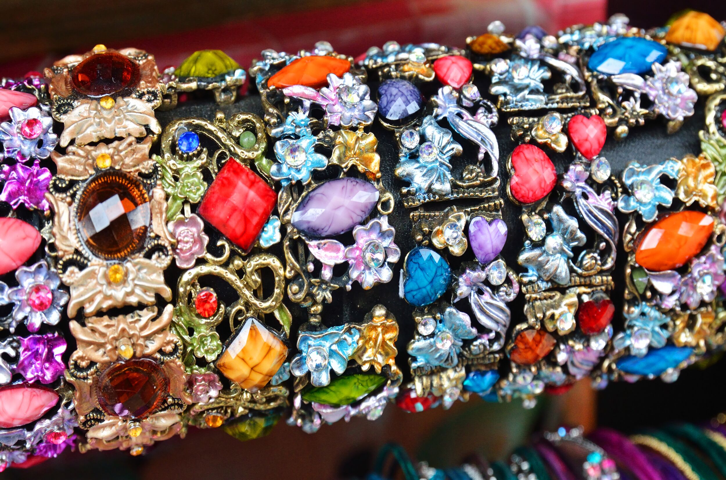 A collection of colorful, ornate bracelets featuring an array of gemstones, floral designs, and intricate metalwork displayed on a dark background.