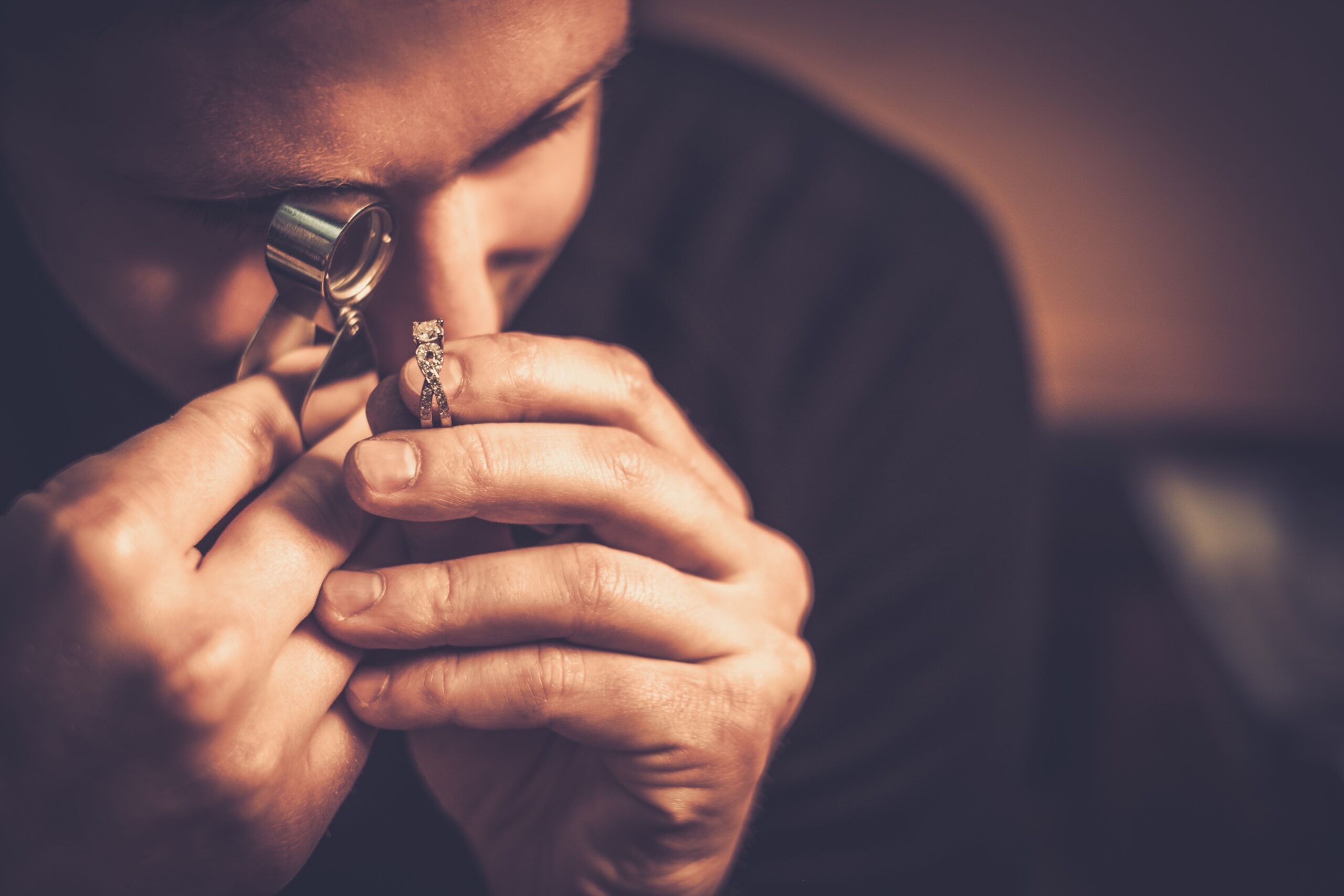 Person examining a diamond ring with a loupe, focusing intently.