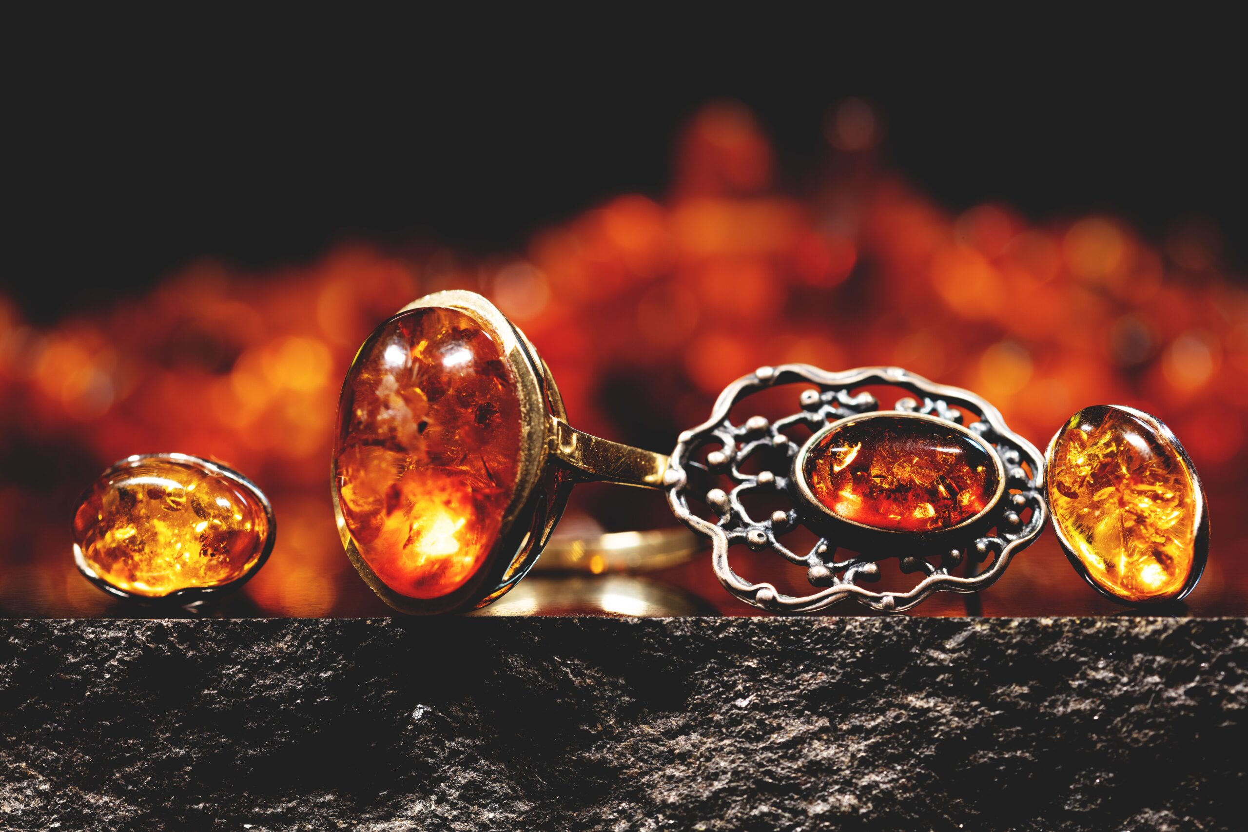Close-up of amber jewelry, including rings with large oval stones and earrings, set against a blurred, warm-toned background, exuding elegance and warmth.