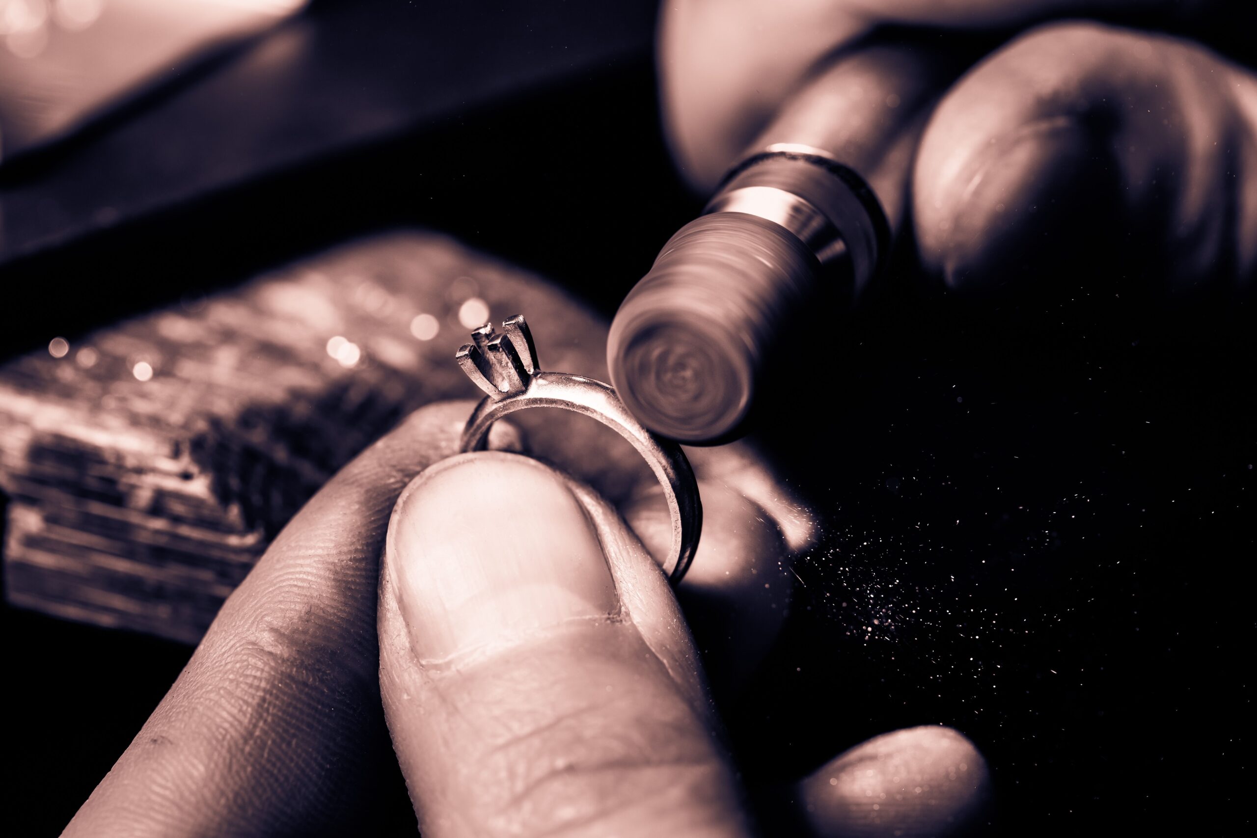 Close-up of hands polishing a silver ring with a tool, under warm lighting.