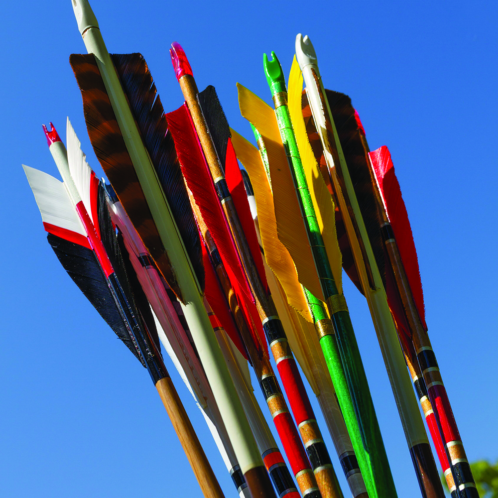 Colorful arrows with varied feather fletching and decorative shafts against a clear blue sky.