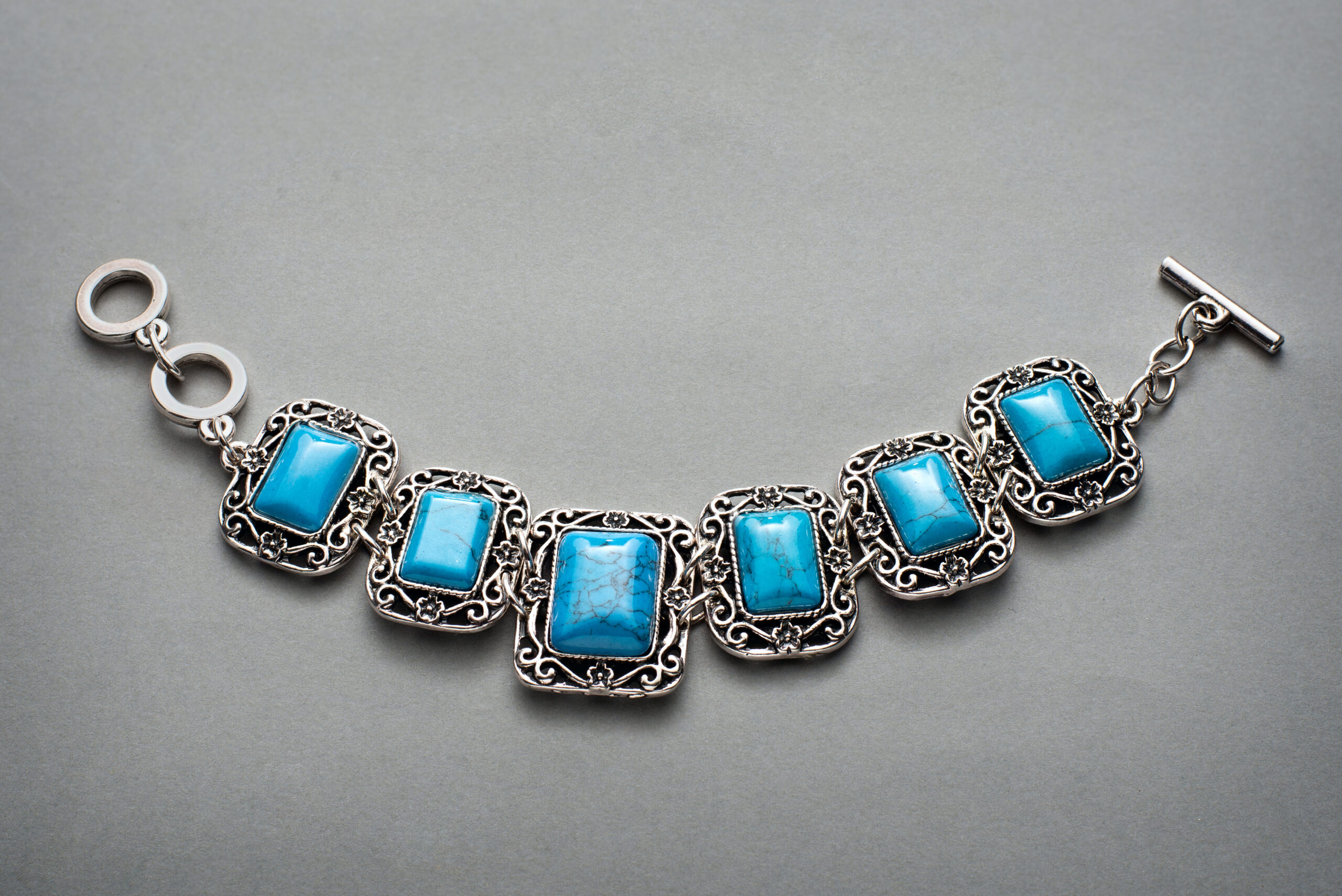Silver bracelet with intricate filigree links and rectangular turquoise stones, creating an elegant and vibrant design on a gray background.